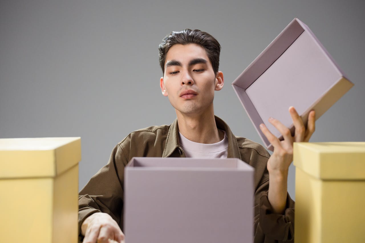 Asian man opening a gift box with a curious expression in a studio environment.